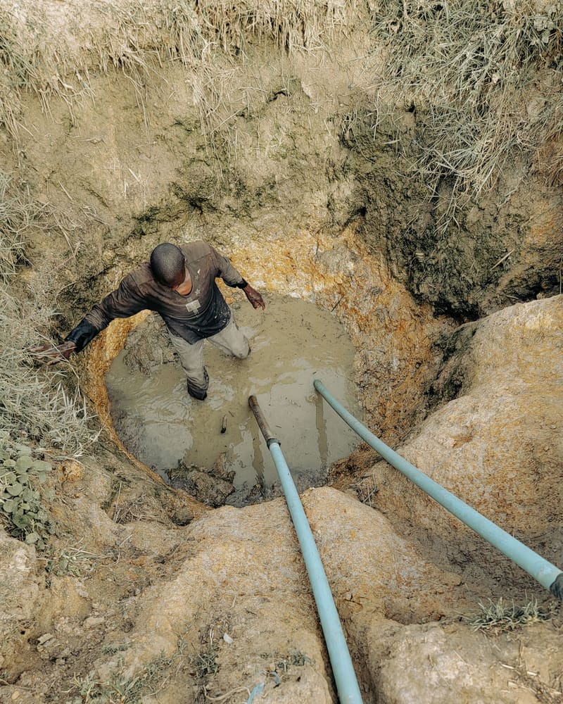 Worker in a muddy excavation trench with exposed pipe during an underground repair